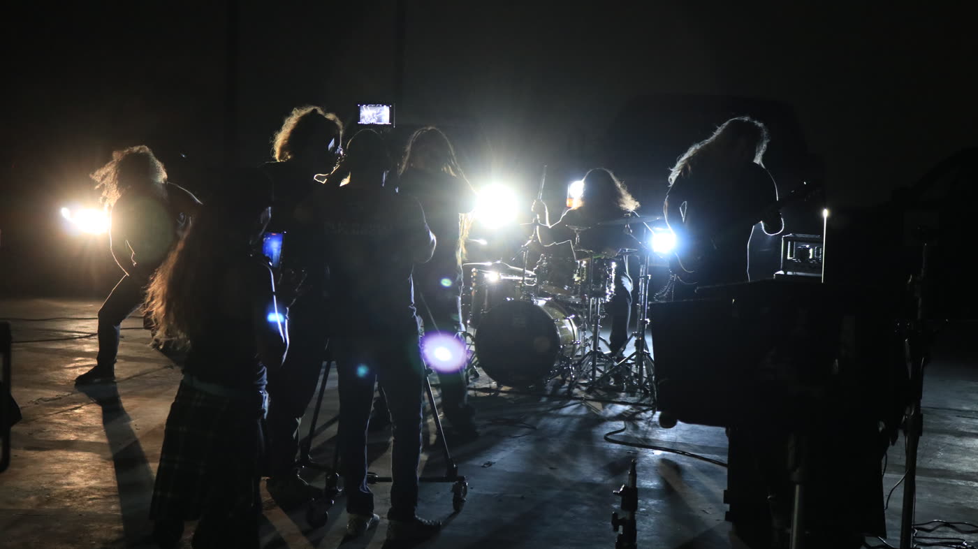 A band lit by headlights on a warehouse music video set