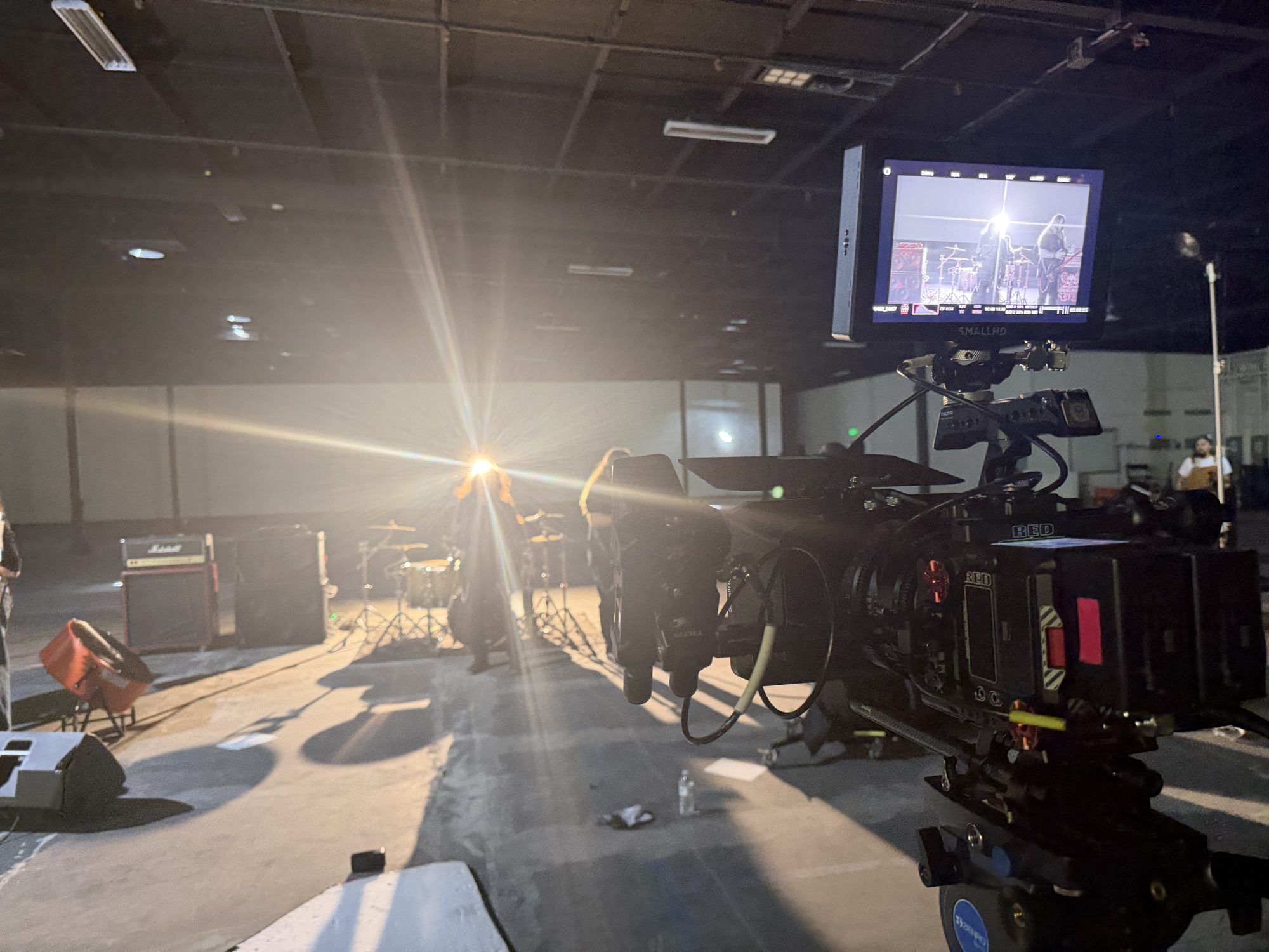RED camera and monitor on a warehouse music video set, lights on the band